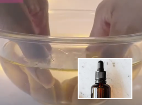 A hand soaking nails in a bowl of warm water mixed with natural oil as a gentle, acetone-free method to loosen nail polish.