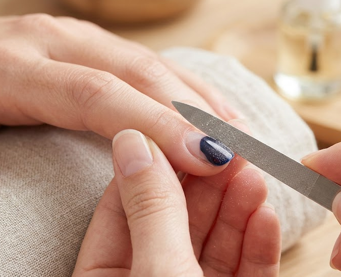 A hand using a nail file to gently buff the top shiny layer of gel polish to break the seal for acetone penetration.