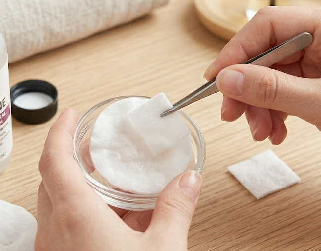 Dampening a cotton ball with acetone for nail polish removal.