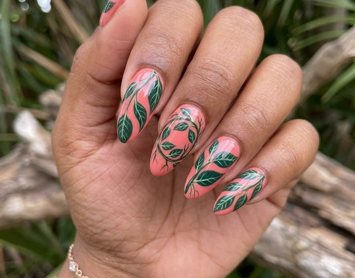 Banyan – Almond shaped nails: Coral pink base, tropical deep green banyan leaves, long flowing trails, glossy summer nails.