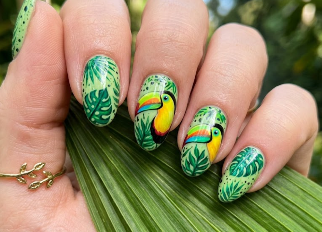 In this picture, almond-shaped nails display colorful toucan beak nail art with tropical leaf patterns.