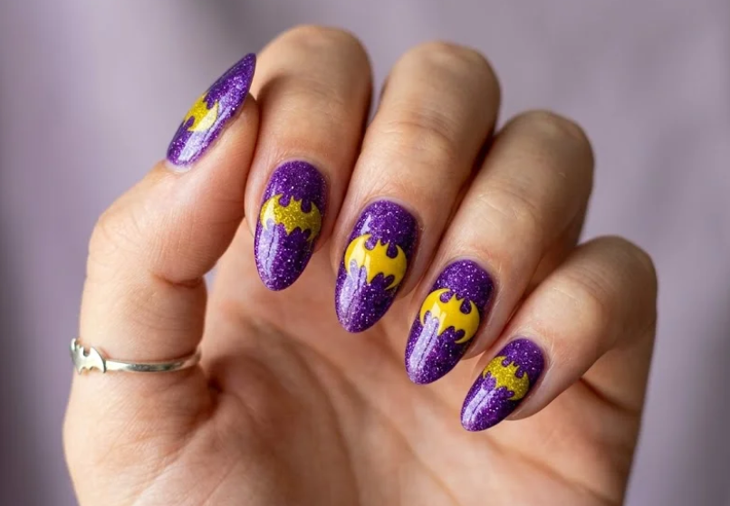 Full hand Batman Batgirl purple glitter nails with yellow bat symbols on a simple background