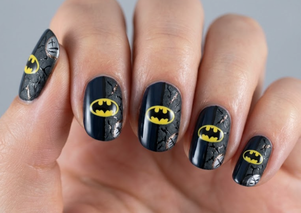 Full hand Batman Two-Face split-style nails with polished and cracked dark textures on a simple background