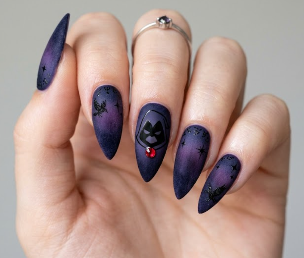 Close-up photo of a sharp stiletto manicure with deep purple velvet texture, showing a clean black silhouette of Raven's hood from Teen Titans and a red gemstone dot.