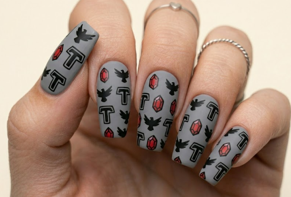 Rounded square nails with a grey base showing a neat pattern of hand-drawn Teen Titans doodles like Raven’s bird logo, her red gem, and the T emblem.