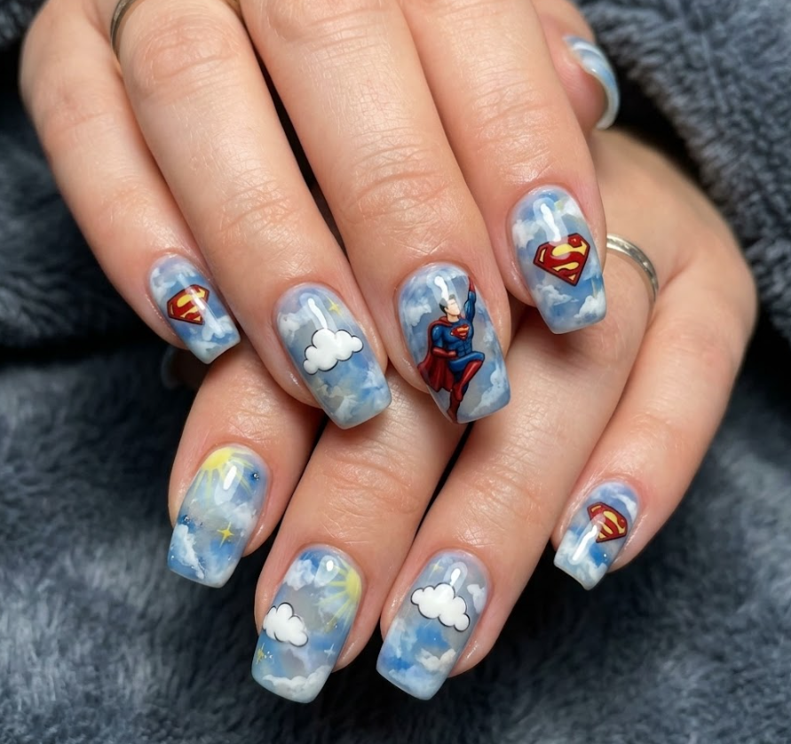 A woman’s hand with sky blue nails, clouds, and a flying Superman illustration on accent nails.