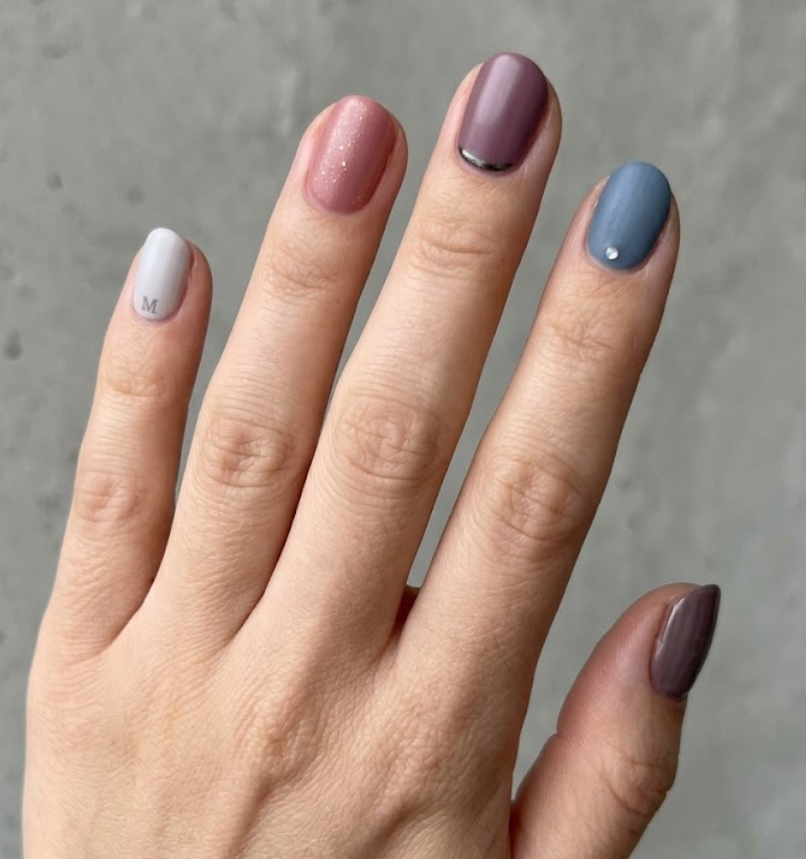 This photo shows full hand Meg Griffin inspired nails with muted emotional tones, subtle bold accents, short rounded nail shape, and simple grey background.