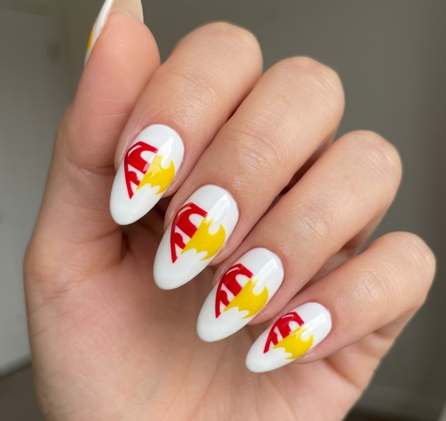 A woman’s hand with white base nails featuring half Superman logo design in red and yellow.