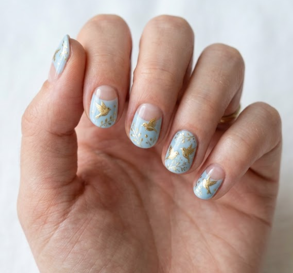 In this picture, short round nails feature golden sparrow nail art with a soft blue base and nude glossy tips.