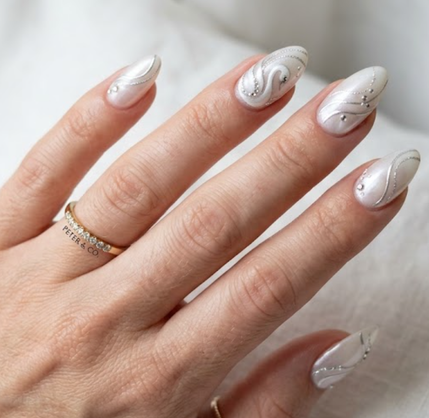 In this picture, almond-shaped nails feature pearl white swan nail art with silver curves and crystals.