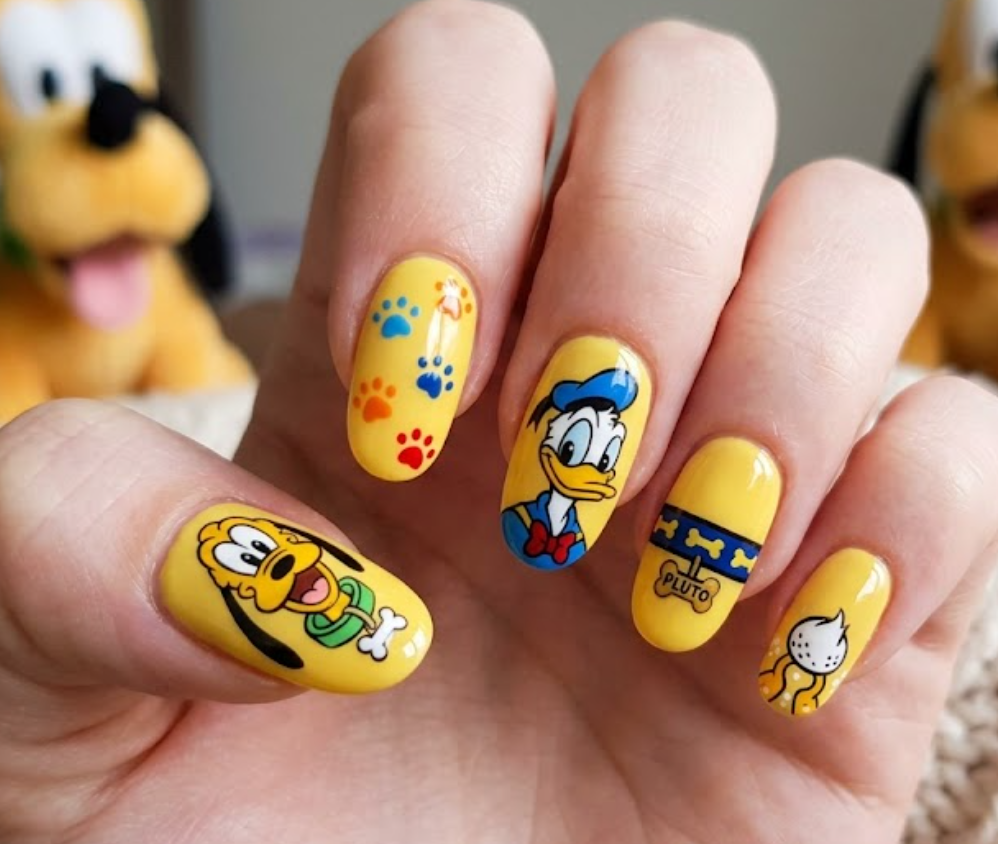 Pluto inspired yellow nail art featuring paw prints, dog collar accents, and cute pet-themed graphics.