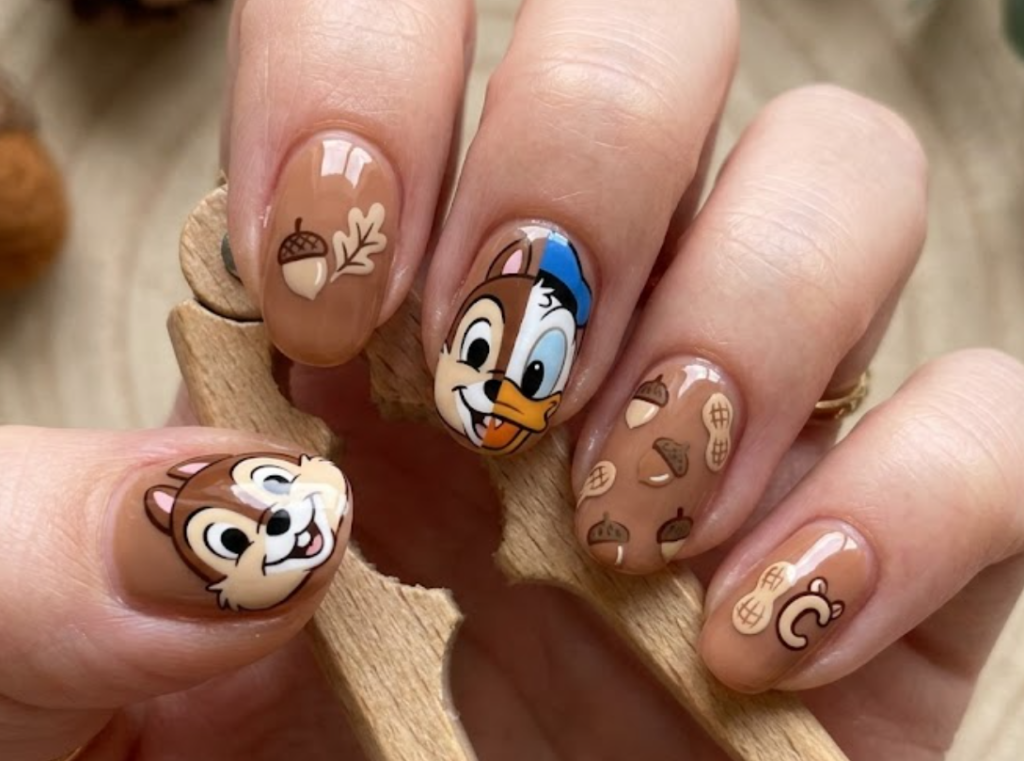 Chip inspired brown nail art featuring nut icons, woodland details, and cute chipmunk-themed graphics.