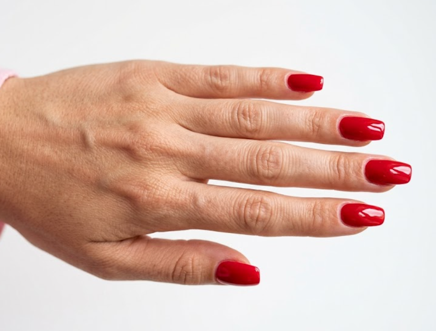 This image shows glossy cherry soda-inspired red summer nails on a female hand with a pastel pink sleeve.