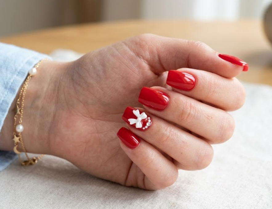 This image shows glossy red nails with tiny bow accents on a female hand wearing a blue sleeve.