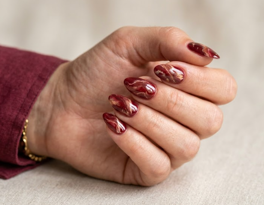 This image shows elegant red marble nail art with soft swirl details on a female hand.