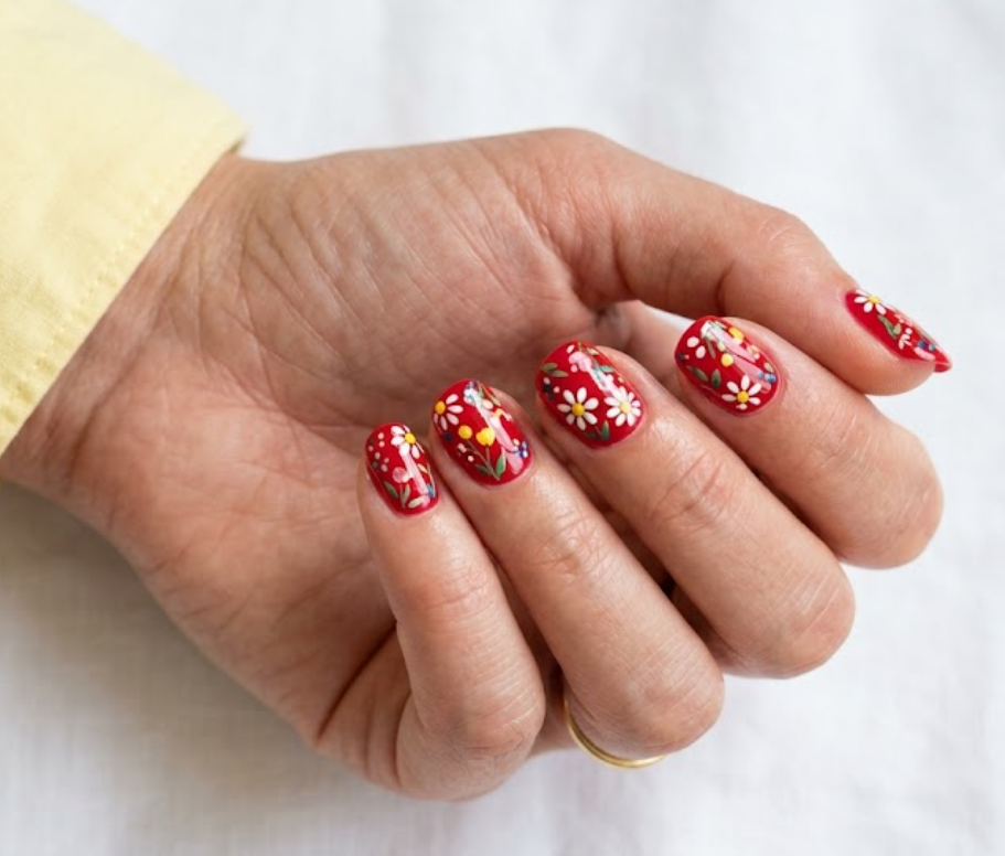 This image shows red nails with delicate floral garden-inspired details on a female hand.