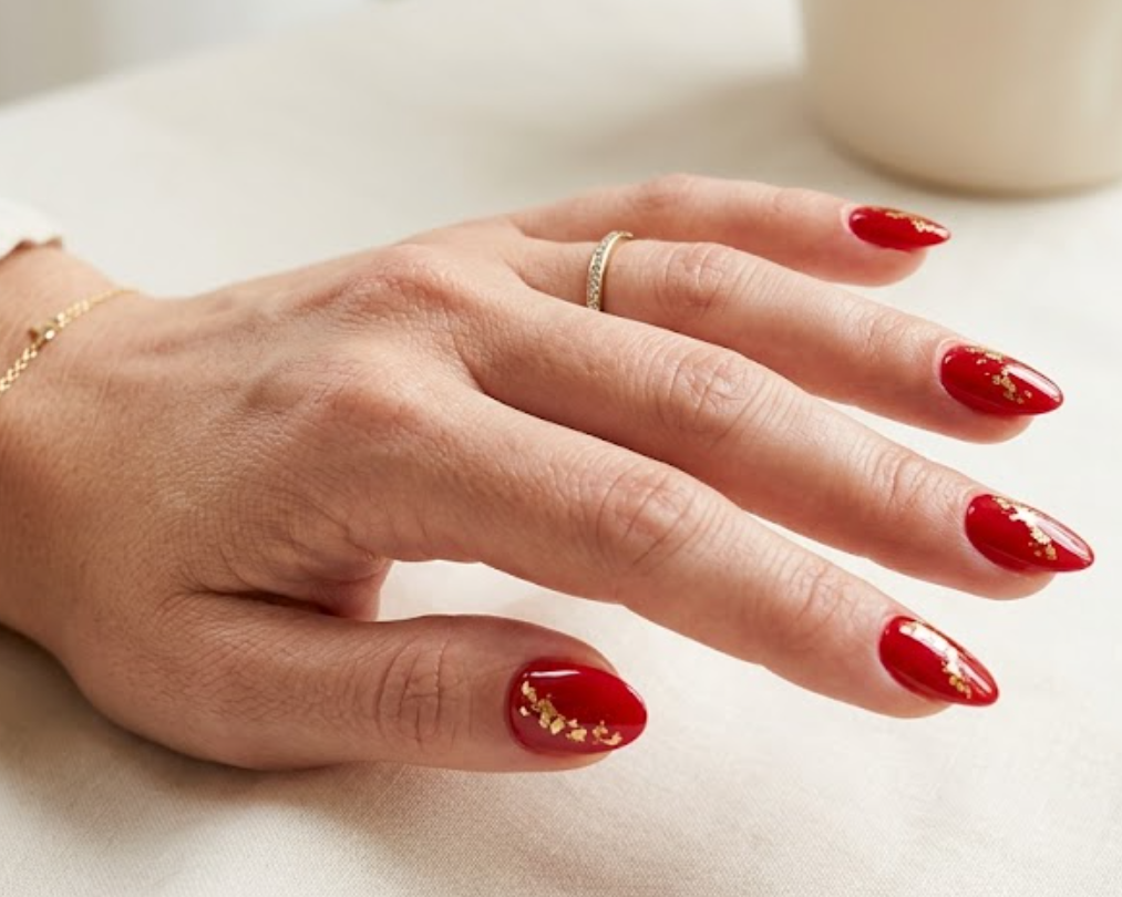 This image shows glossy red nails with subtle gold accents on a female hand wearing a cream sleeve.