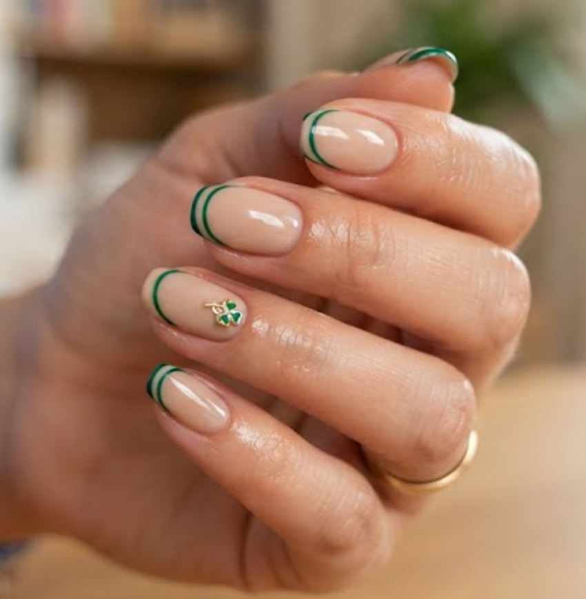 In this image, clean nails feature double French tips and a clover charm while wearing a sky blue shirt.