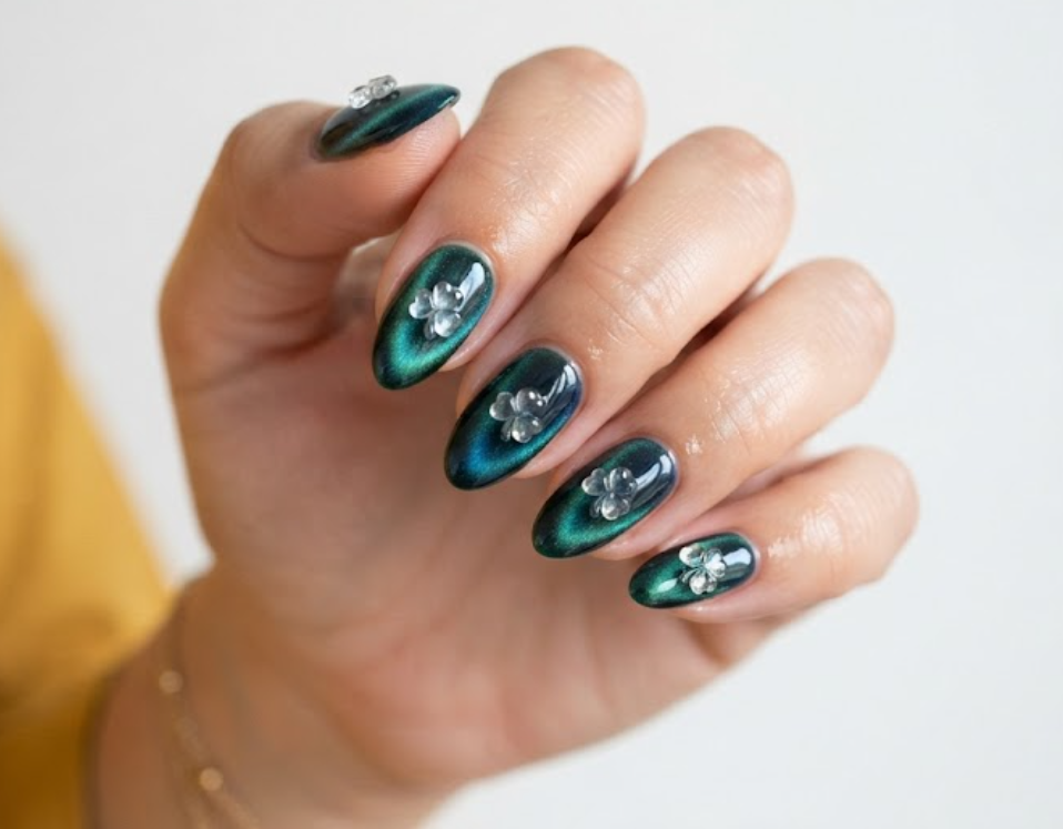 In this image, clean nails show velvet cat-eye emerald polish and glossy clovers while wearing a mustard shirt.