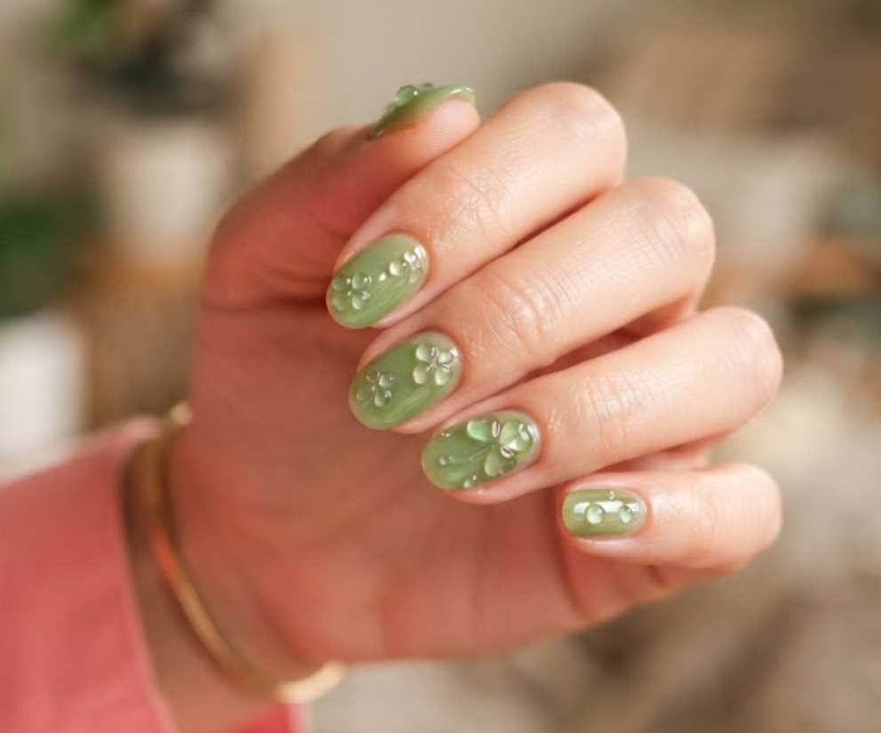 In this image, clean nails feature transparent jelly green polish and 3D gel clovers while wearing a coral shirt.