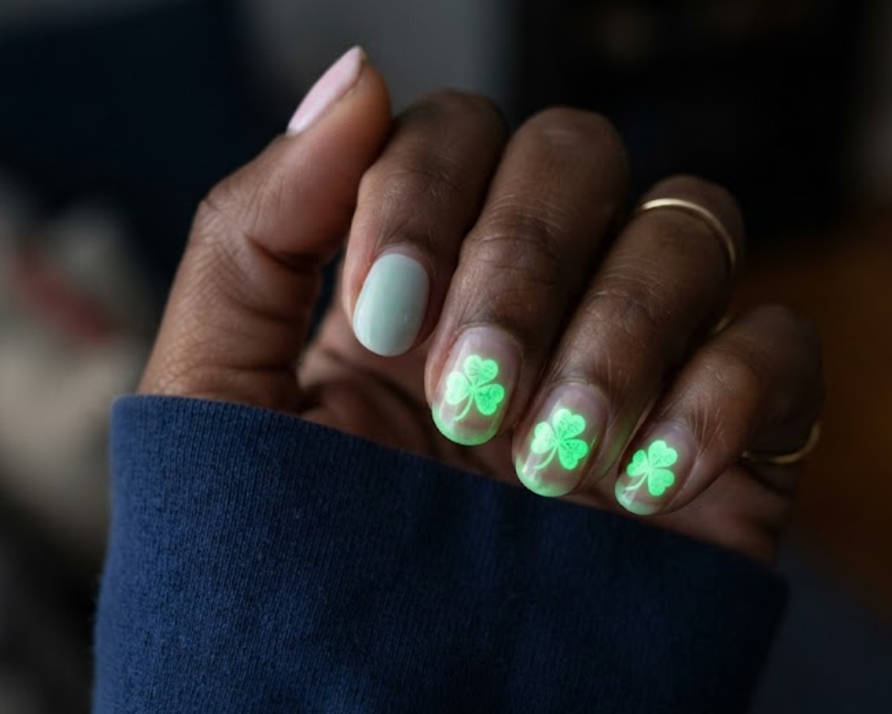 In this image, a glowing 4-Leaf Clover Nail features pastel polish transforming into vibrant green clover art with a navy blue shirt.