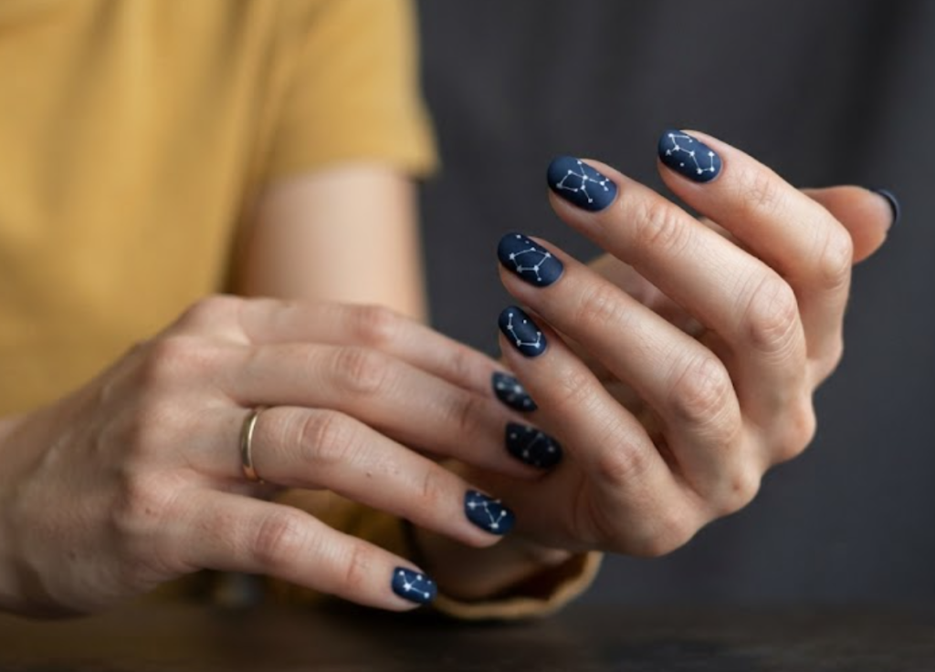 in this image real hands display a minimalist constellation map camp nail design. camp inspired nail design