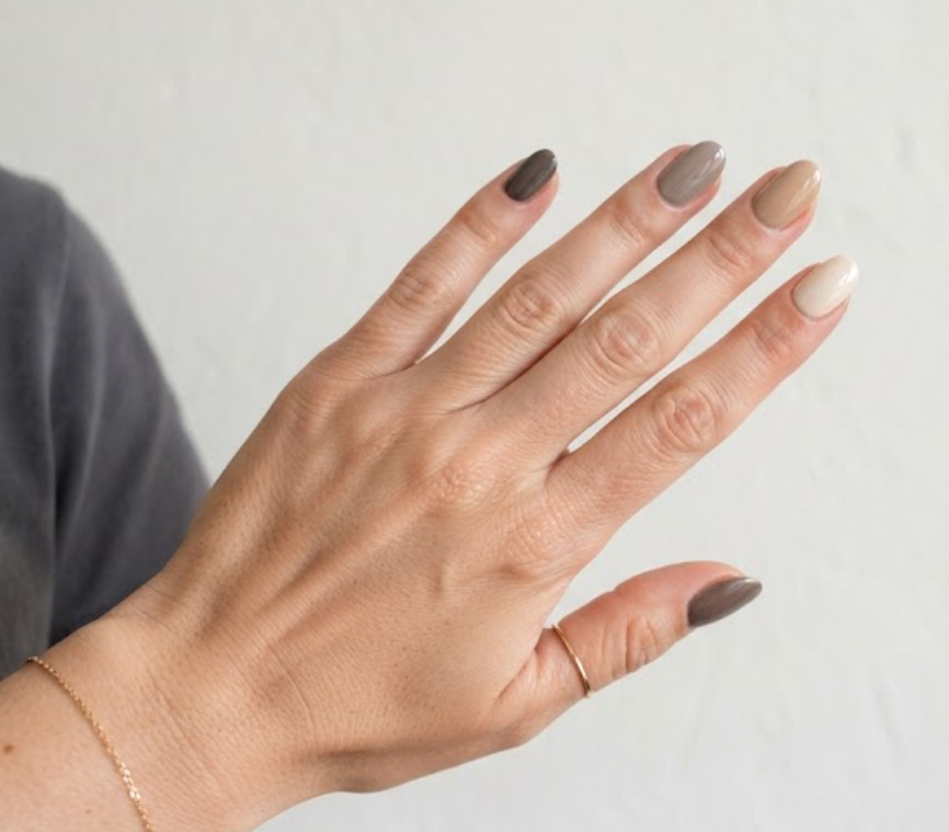 In this image, a full hand with extremely short oval nails displays business nails with taupe-to-sand gradient tones, wearing a charcoal grey shirt.