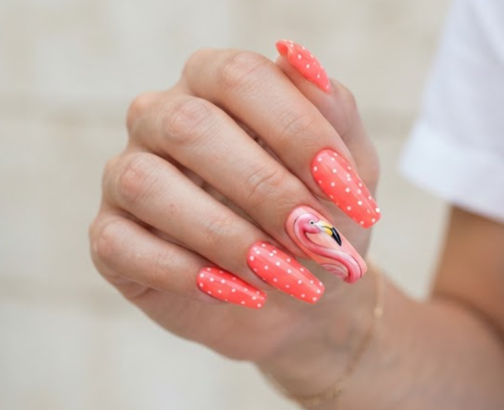 In this image, a woman in a white blouse features long coffin nails with a coral base, flamingo neck art, and polka dots.