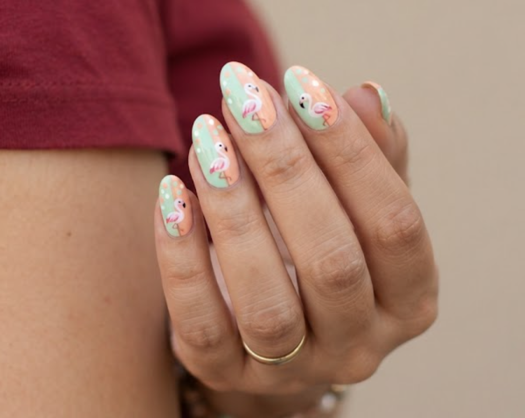 In this image, a woman in a maroon tee presents medium almond nails with a vertical split mint-and-peach base and flamingo.