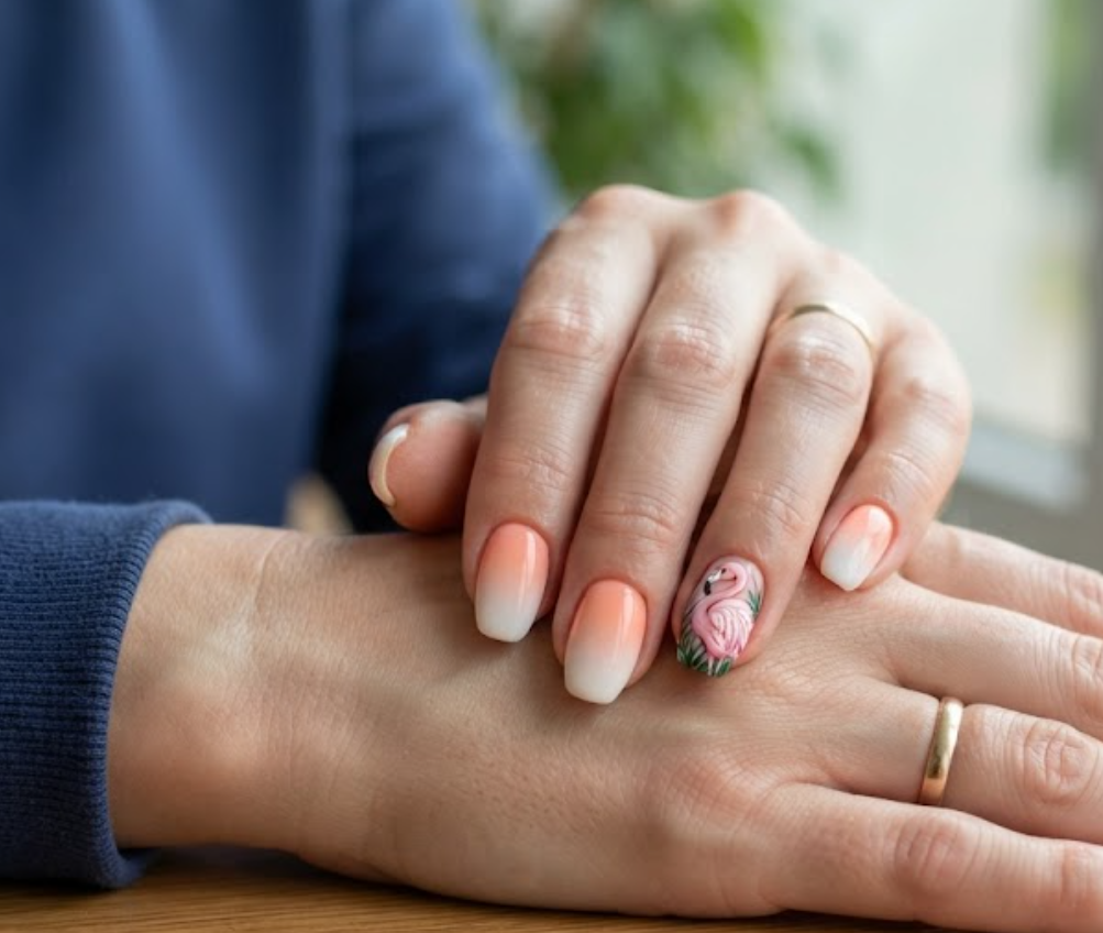 In this image, a woman in a navy sweatshirt showcases medium ballerina nails featuring a peach ombre base and detailed flamingo.