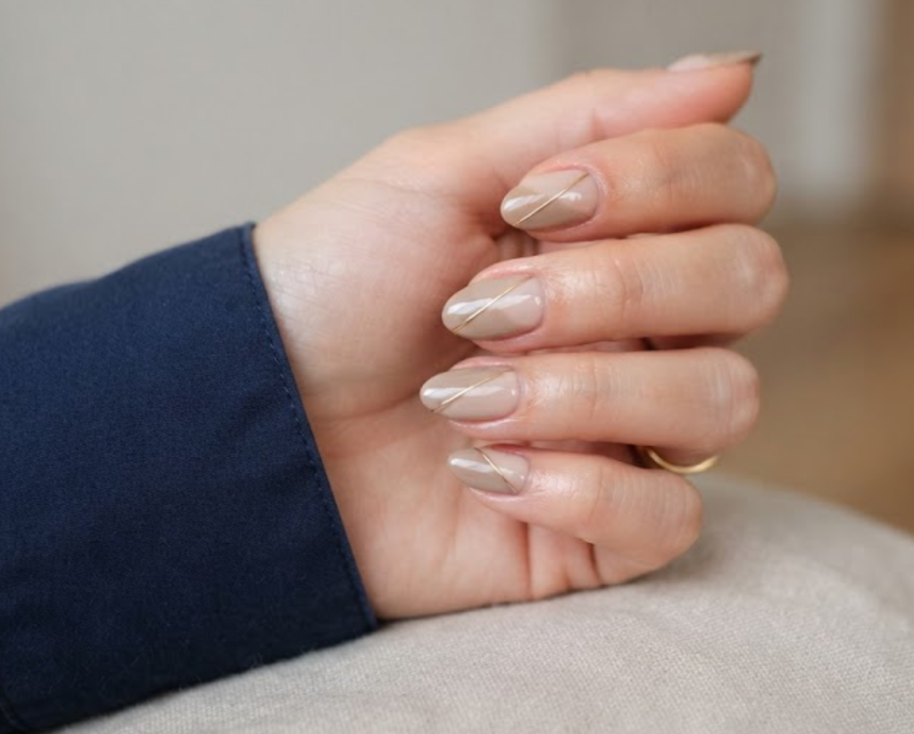 In this image, full hands with short almond nails feature a single gold wire across a taupe split-gradient against a minimalist indoor background.