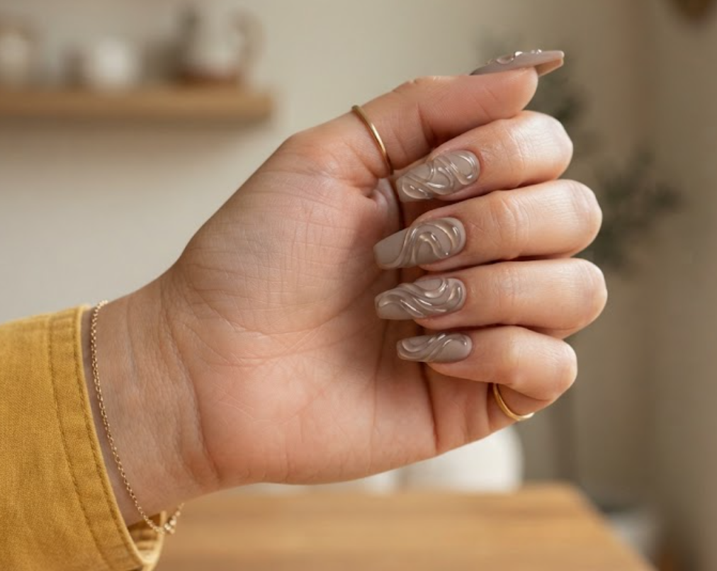 In this image, full hands with coffin nails showcase glossy transparent jelly ribbons on matte taupe against a clean room background.