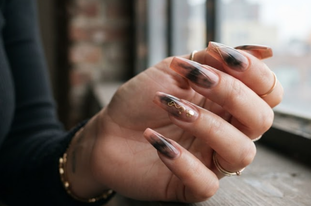 In this image, full hands with long coffin nails feature a smoky charcoal and taupe smudge gradient against an industrial loft background.