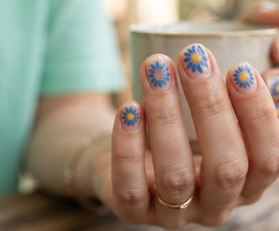 In this image, real hand nails exhibit a clear base with stencil blue sunflowers and a mint green shirt.