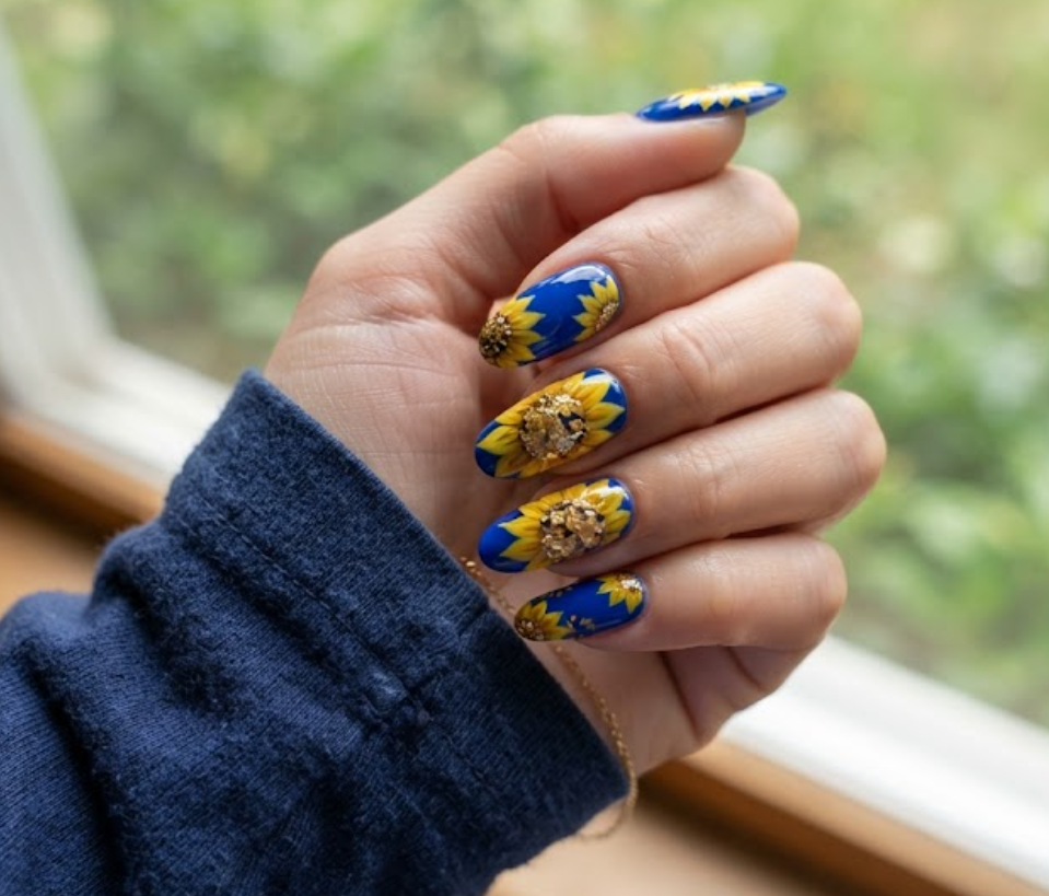 In this image, real hand nails present a cobalt blue base with gold foil sunflower petals and a navy shirt.
