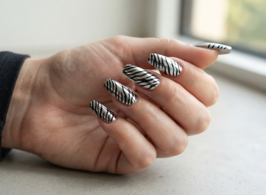 In this image, a close-up of coffin animal nails displaying a metallic silver and black zebra print pattern, paired with a black shirt.