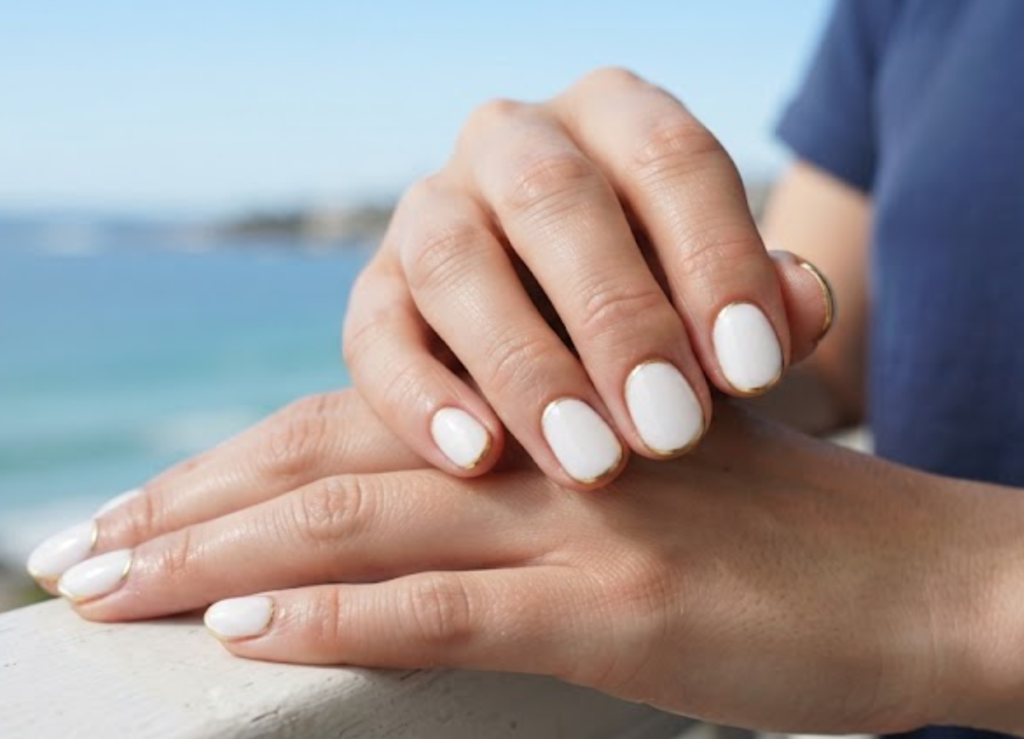 In this image, cruise wedding nails highlight short round glossy white nails with metallic gold tip outlines, worn by hands in a navy shirt.