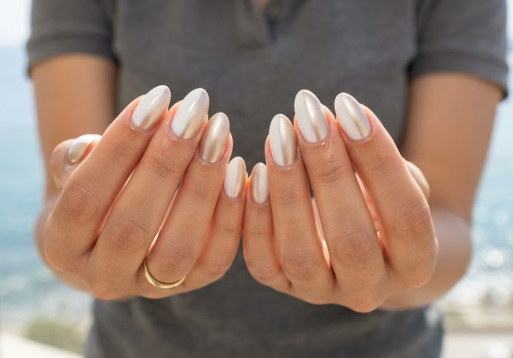 In this image, cruise wedding nails display short almond nails with milky white and champagne gold blocks, worn by hands in a charcoal polo.