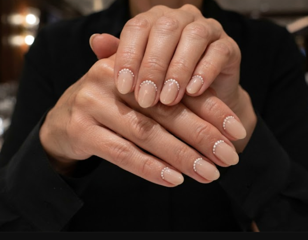 In this image, cruise wedding nails feature short oval sheer nude nails with micro-pearl cuticles, worn by hands in a black dress shirt.