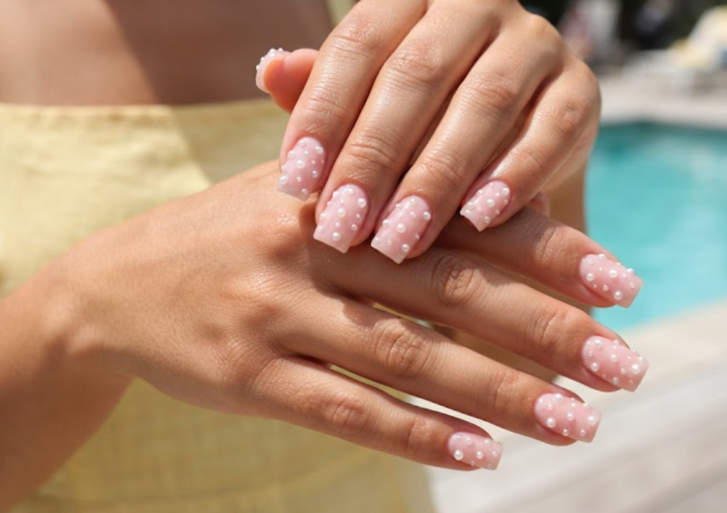 In this image, cruise wedding nails present short square pink jelly nails with scattered caviar pearls, worn by hands in a yellow sundress.