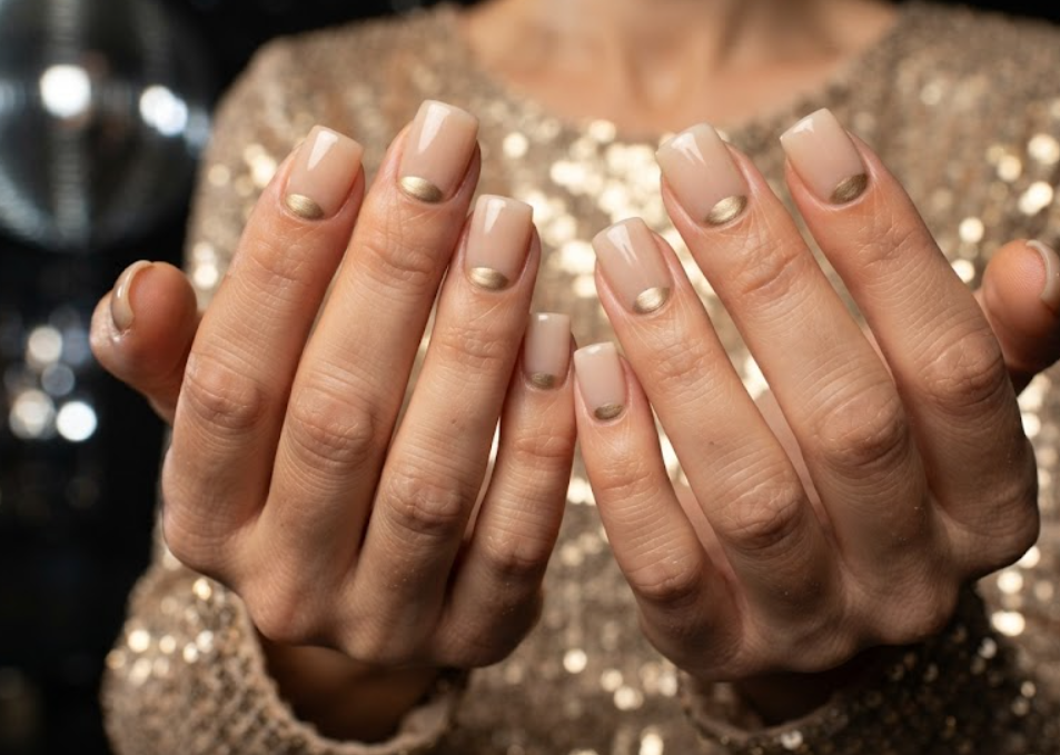 In this image, cruise wedding nails highlight short square reverse French nails with a gold half-moon, worn by hands in a gold sequin top.