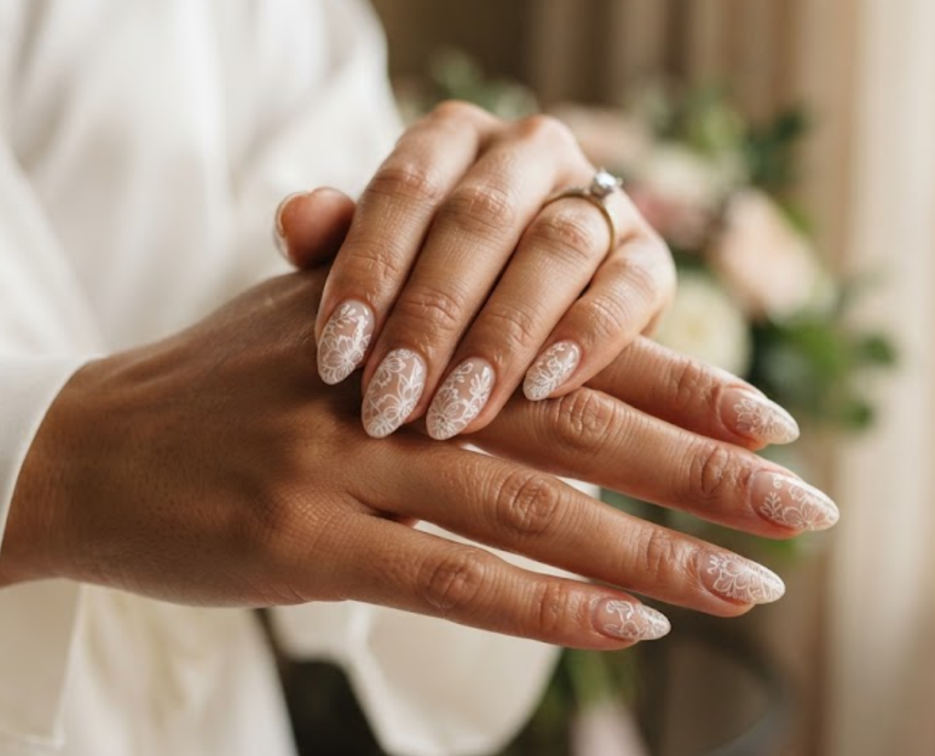 In this image, cruise wedding nails feature short almond sheer nude nails with fine-line lace florals, worn by hands in an ivory bridal robe.