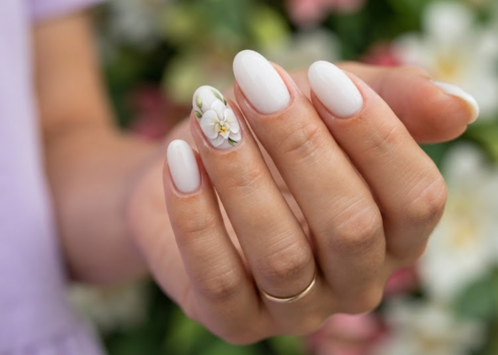 In this image, cruise wedding nails display short oval milky white nails with an accent white orchid, worn by hands in a soft lilac dress.