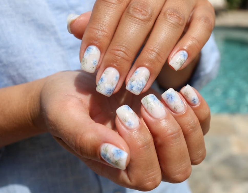 In this image, cruise wedding nails highlight short squoval milky nails with watercolor blue petals, worn by hands in a pale blue blouse.