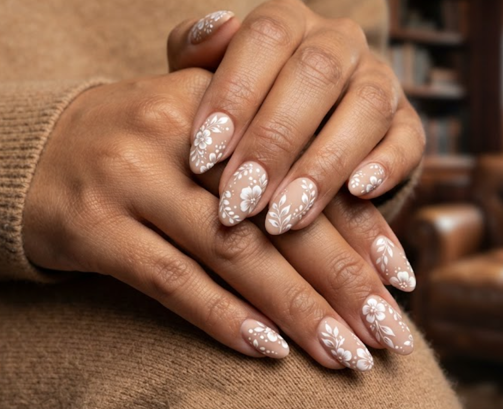 In this image, cruise wedding nails highlight short almond matte nude nails with glossy white florals, worn by hands in a tan sweater.
