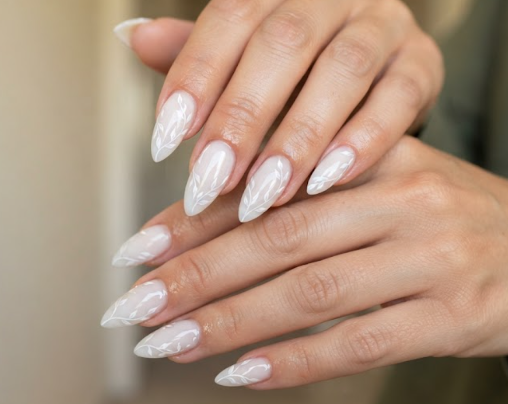 In this image, cruise wedding nails display short stiletto milky nails with side-winding white vine art, worn by hands in an olive green blouse.