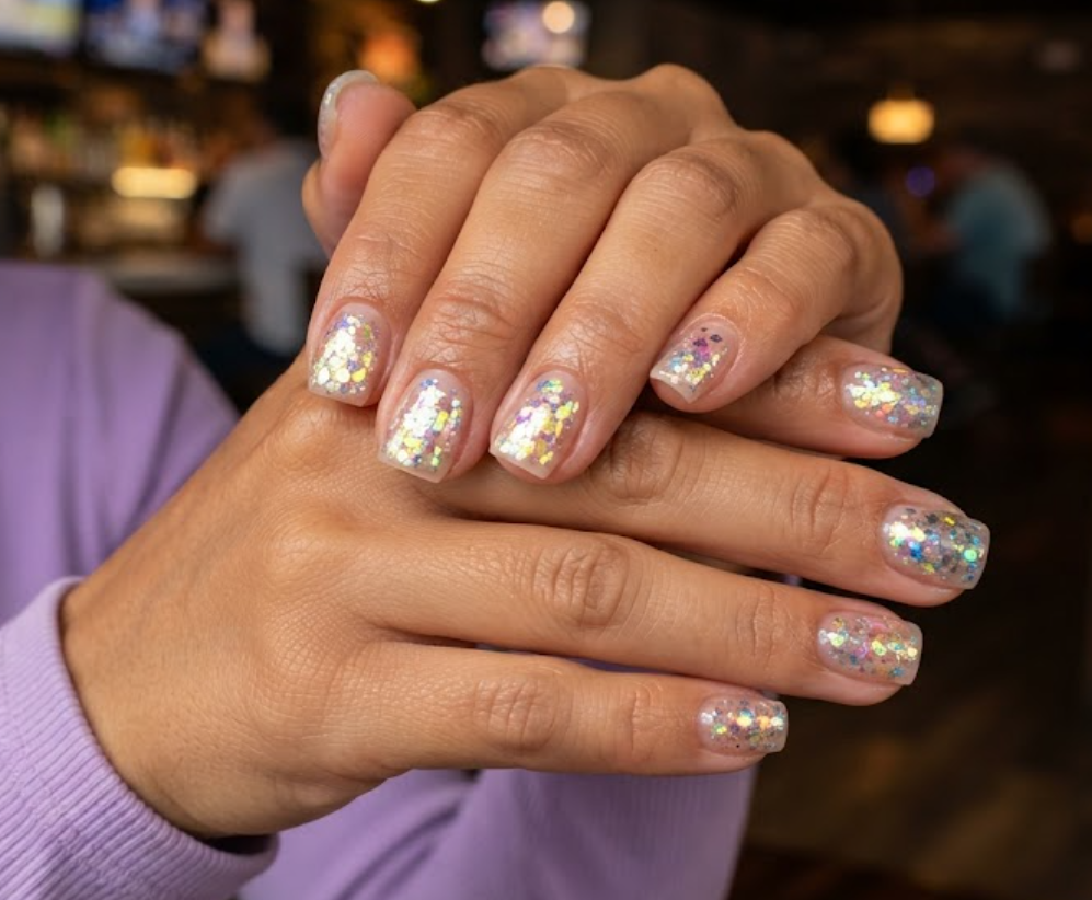 In this image, cruise wedding nails show short square clear nails with chunky iridescent holographic flakes, worn by hands in a lavender top.