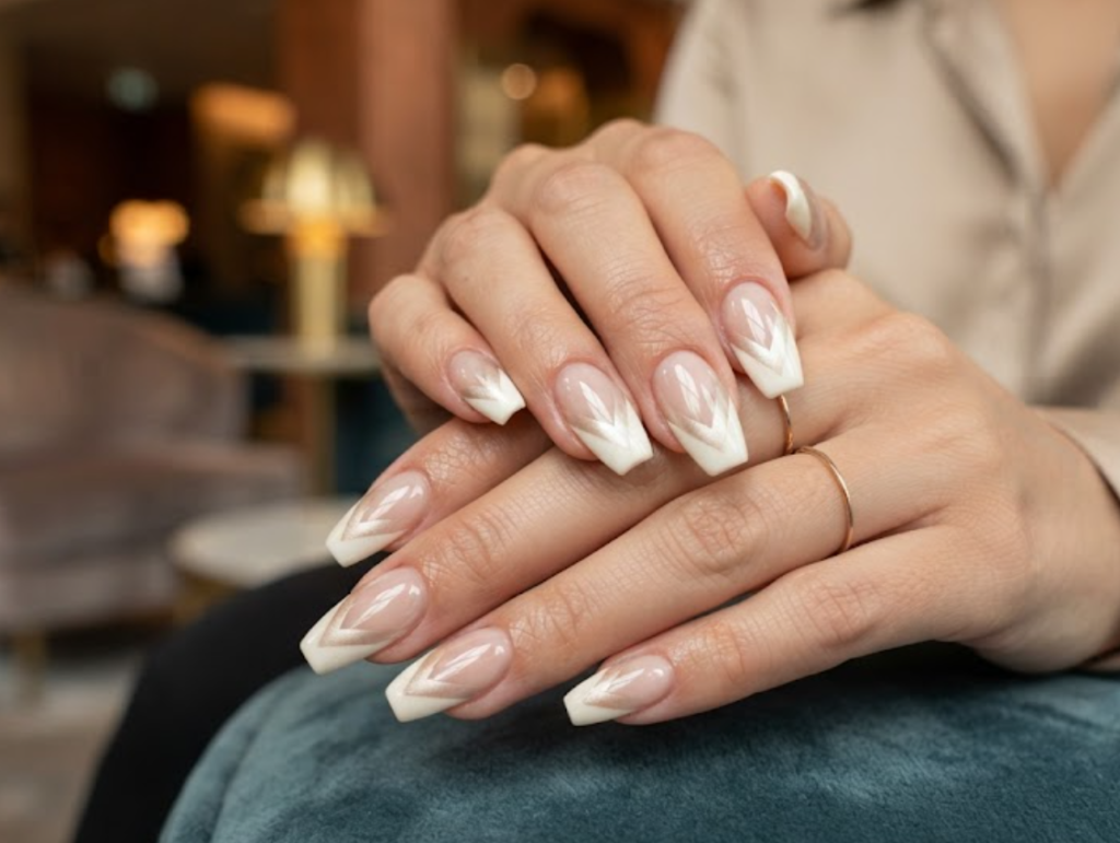 In this image, cruise wedding nails display short coffin nude nails with modern ivory and champagne chevron tips, worn by hands in a champagne shirt.