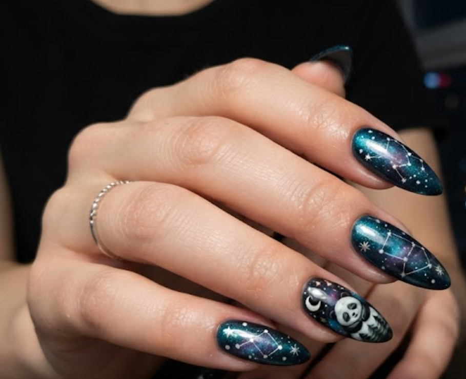 In this image, stiletto nails with a dark teal shimmer base and galaxy nebula effect are shown. The accent nail shows a sleeping panda under a starry sky. Others feature constellation star maps, nebula blends, and silver floating glitter dots. The hand wears a black shirt against a night window view.