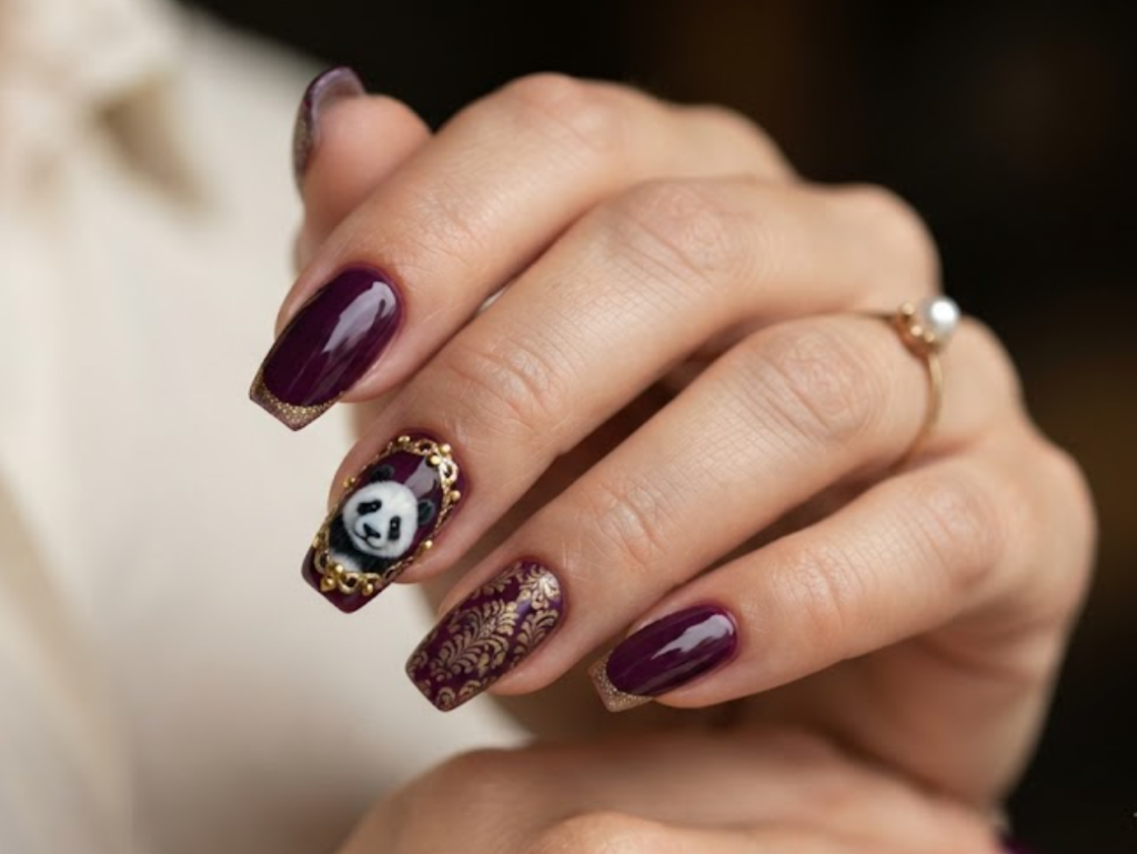 In this image, coffin-shaped nails with a deep royal plum base are highlighted. The accent nail has a gold-framed panda face portrait. Others feature gold glitter French lines, royal damask lace patterns, and solid deep plum nails. The hand wears a cream blouse.